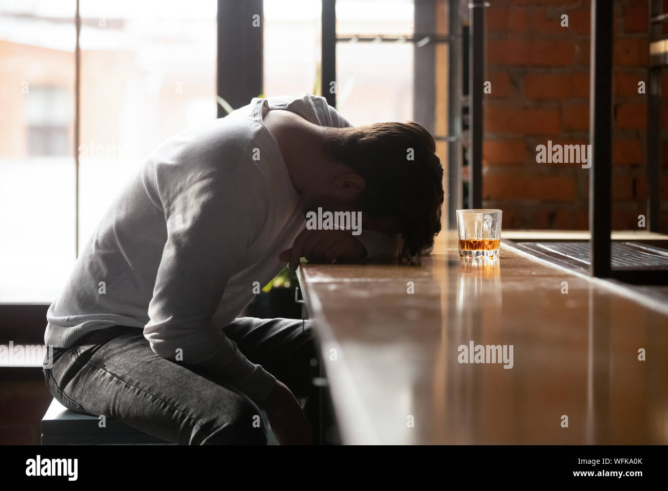 Depressed drunk young addicted man drinker sleeping alone in bar Stock Photo