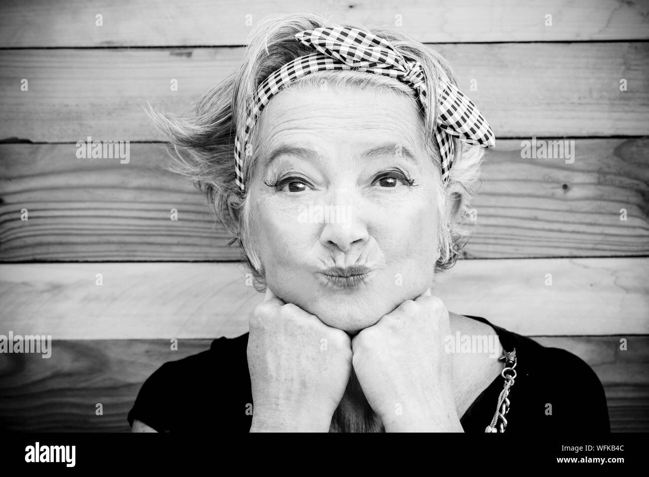 senior and mature woman with makeup is looking at the camera - funny moment with a wood table at the background - cheerful old lady go crazy and nice Stock Photo