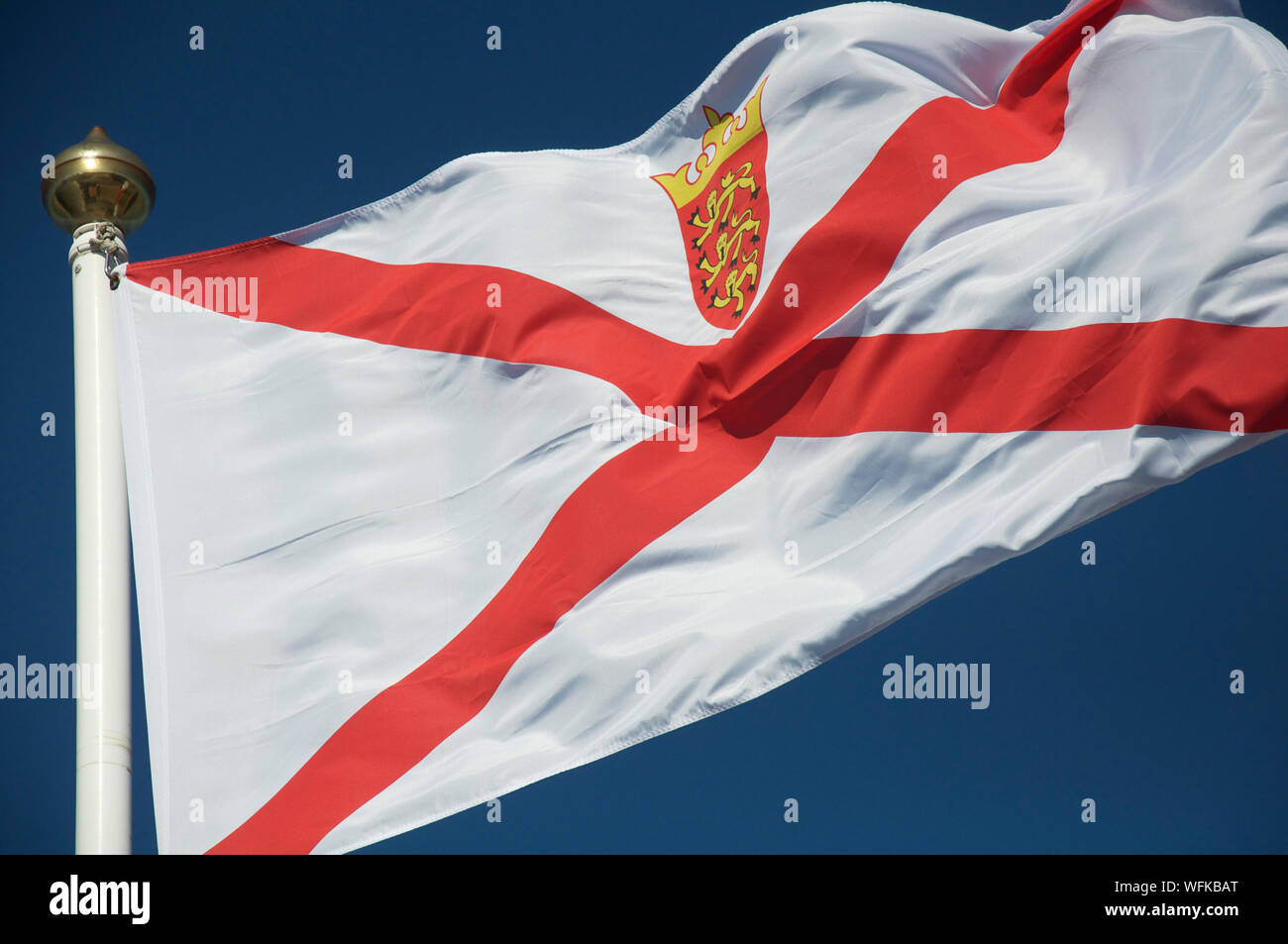 The flag of the States of Jersey blowing in the wind against a blue sky. The Bailiwick of Jersey is the largest of the Channel Islands. British Isles. Stock Photo