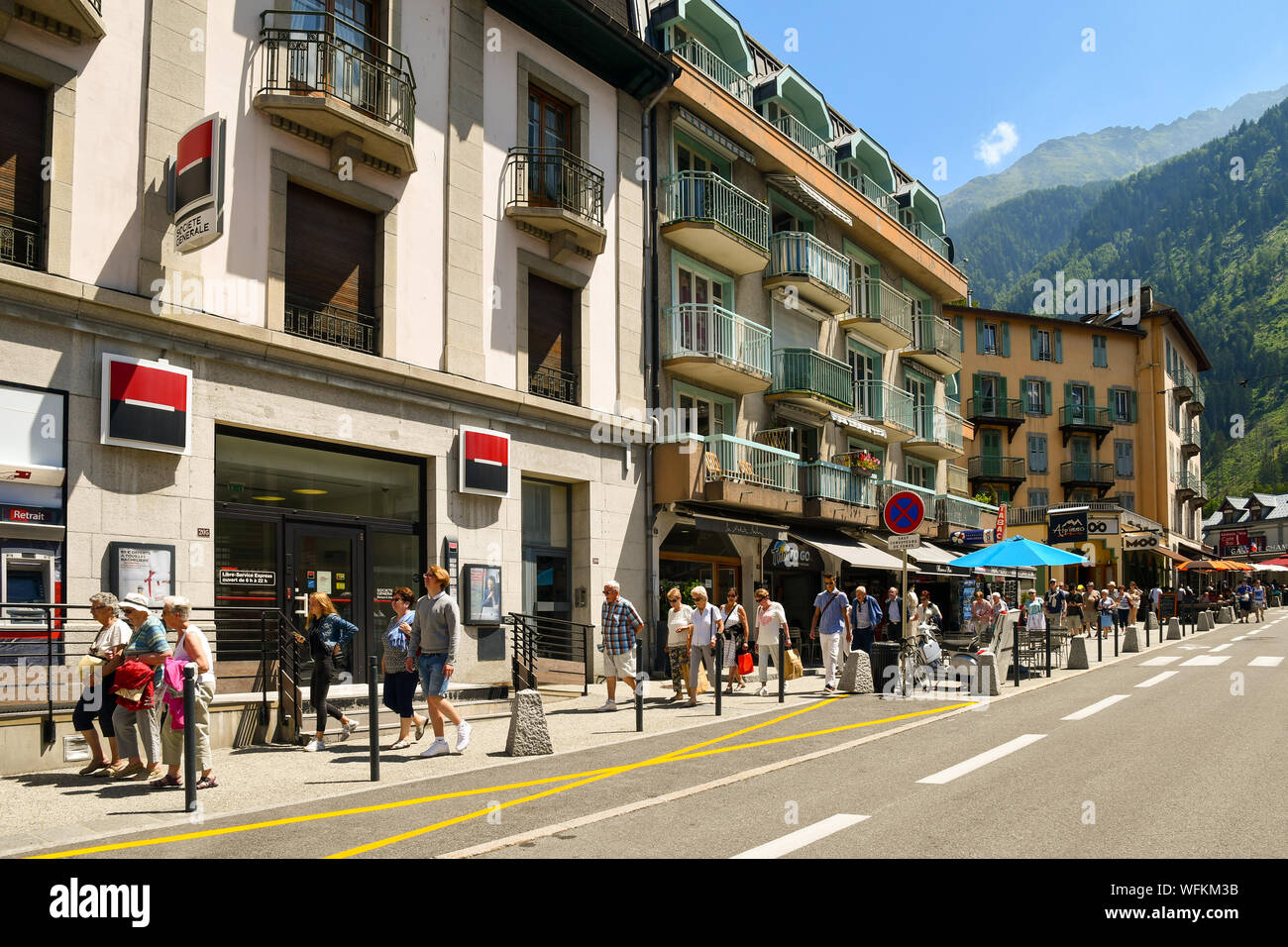 Street view of the historical centre with people and tourists walking on the sidewalk and the mountains in the background in summer, Chamonix, France Stock Photo