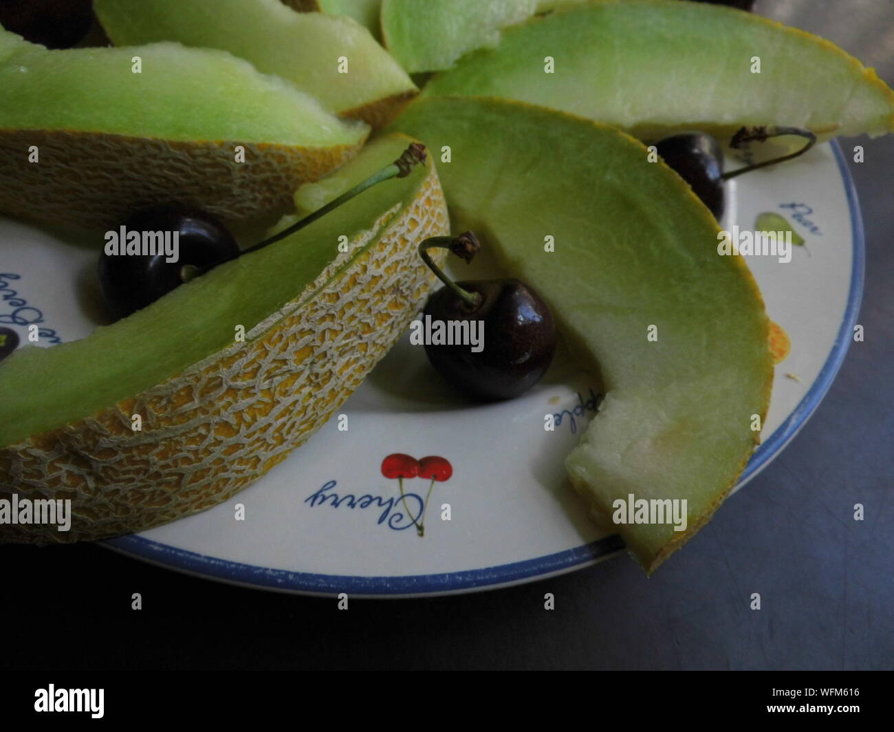 High Angle View Of Honeydew Melon And Black Cherry Fruits In Plate Stock Photo