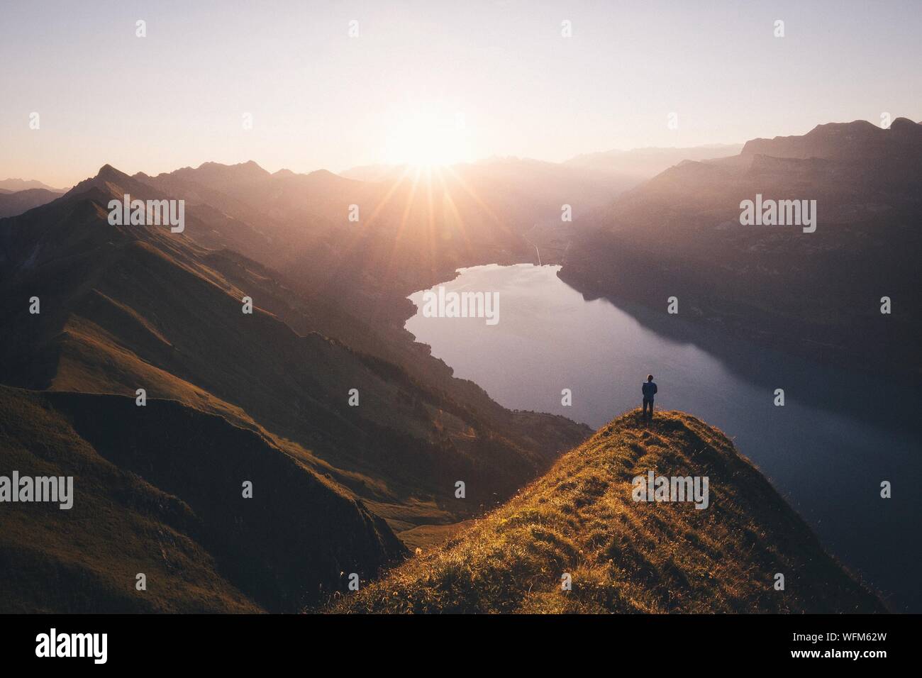 Man Standing On Cliff Looking Down On Mountain Lake Stock Photo