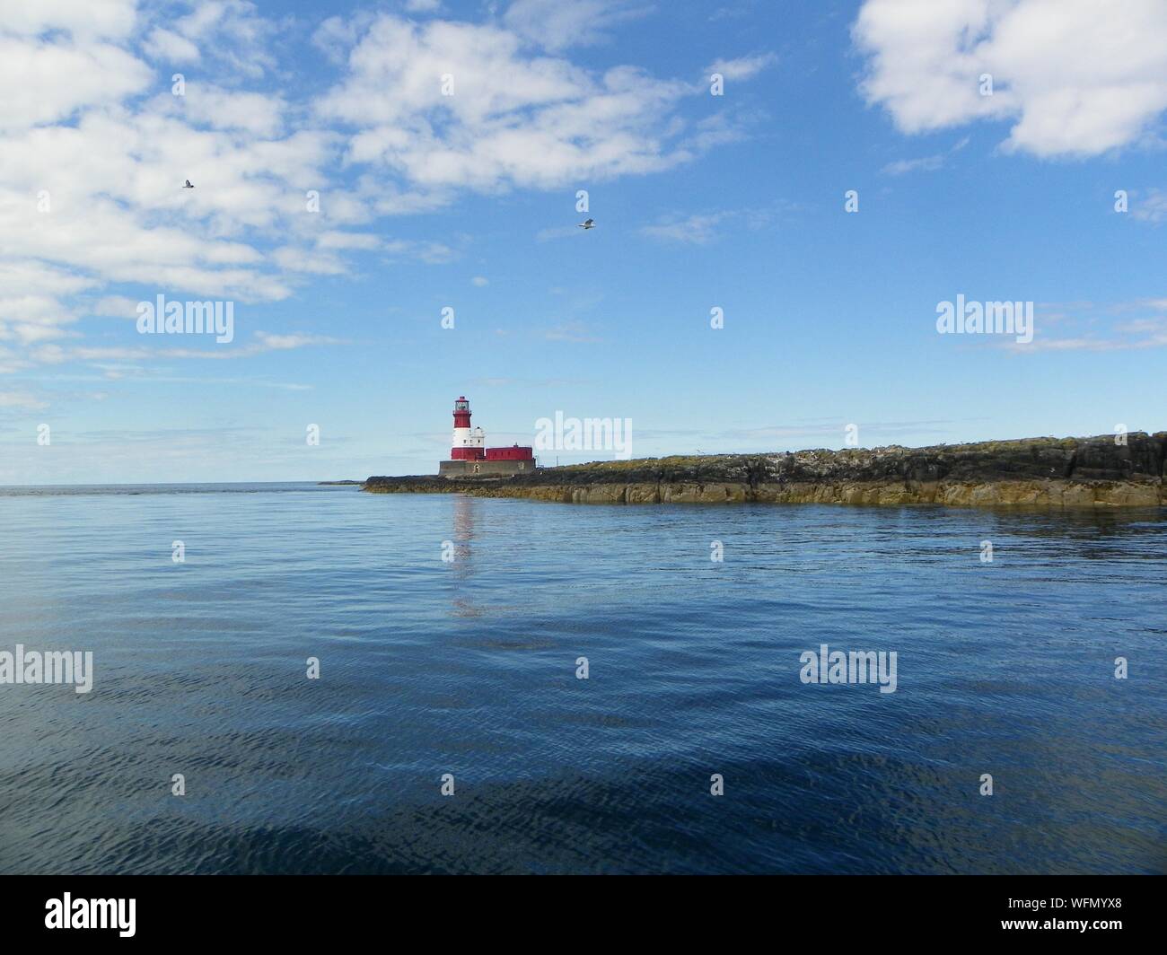 Longstone Lighthouse By Sea Against Cloudy Sky Stock Photo