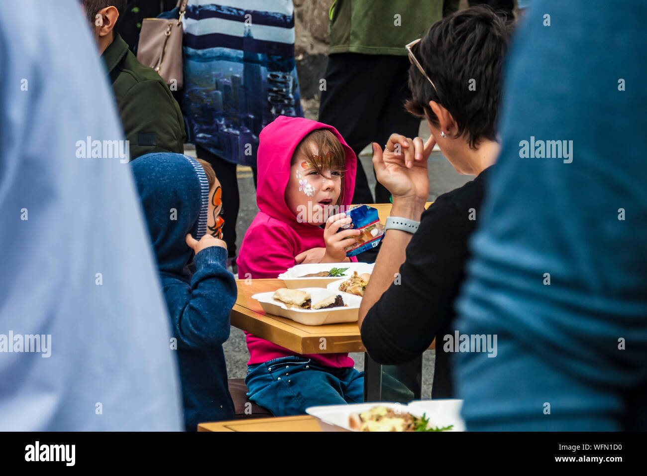Family with kids eating at the street table in crowd. Dalkey, Dublin, Ireland.25 August 2019.  Seafood “Dalkey Lobster Festival” Stock Photo