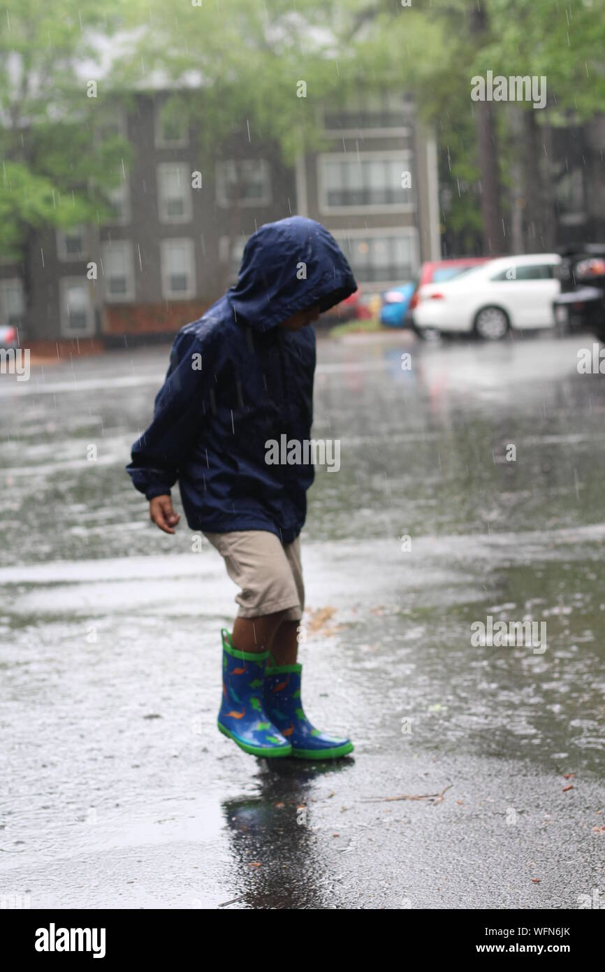 Boy In Raincoat Standing On Street During Rainfall Stock Photo