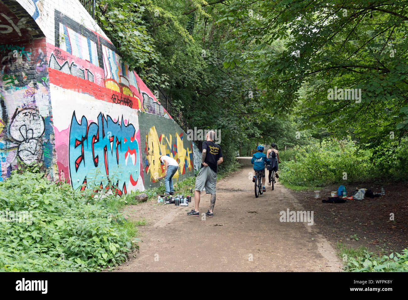 Graffiti artist at work with passing cyclists Parkland Walk, a disused railway line now an urban nature reserve London Borough of Islington Stock Photo