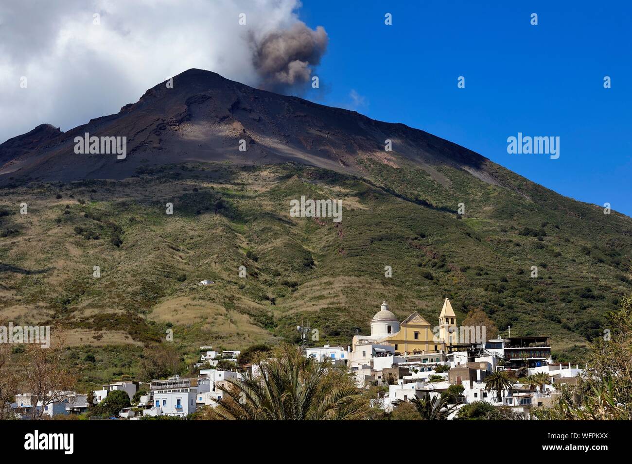 Italy, Sicily, Aeolian Islands, listed as World Heritage by UNESCO, Stromboli island, one of the multiple and regular eruptions of the Stromboli volcano which rises to 924m, Chiesa di San Vincenzo (St. Vincent Church) in the village of Stromboli in the foreground Stock Photo