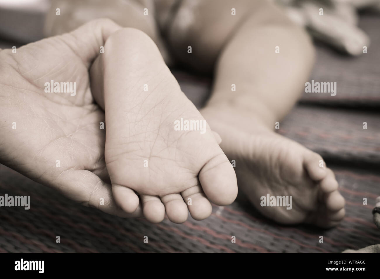 Cropped Hand Holding Baby Feet On Bed Stock Photo