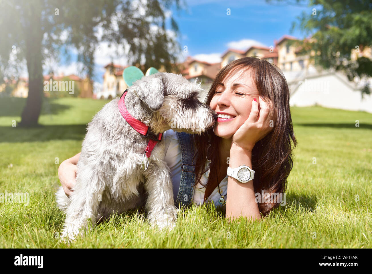 Pretty adult caucasian happy woman resting in the park on a sunny day with her beloved dog. Female lay on the grass smiling and looking at the camera Stock Photo
