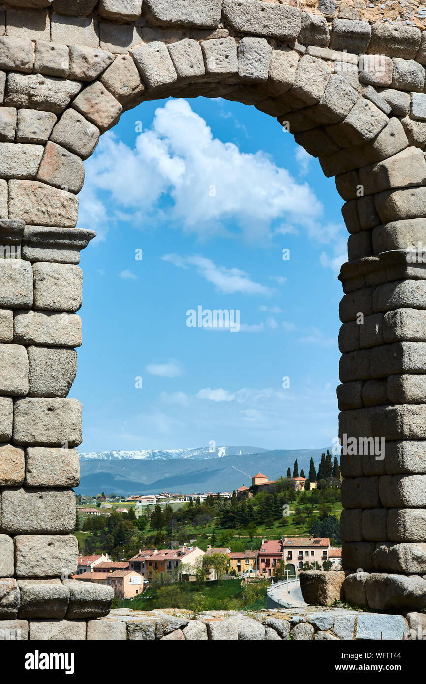 SEGOVIA, SPAIN - APRIL 25, 2018: Landscape with green trees and snowy peaks under amazing blue sky seen through one of the arches of the Roman Aqueduc Stock Photo
