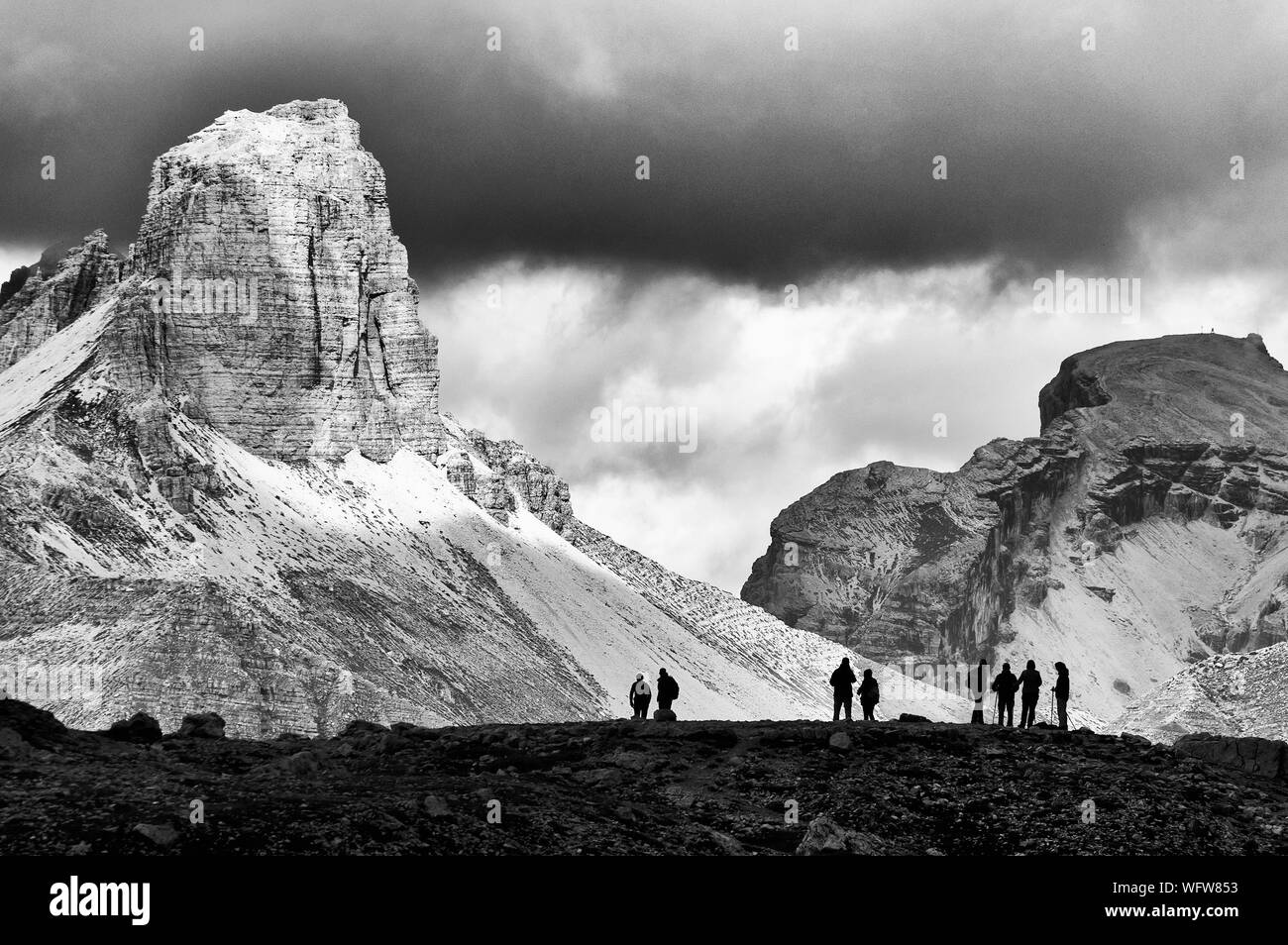People On Cliff Against Rocky Mountains At Dolomites Stock Photo