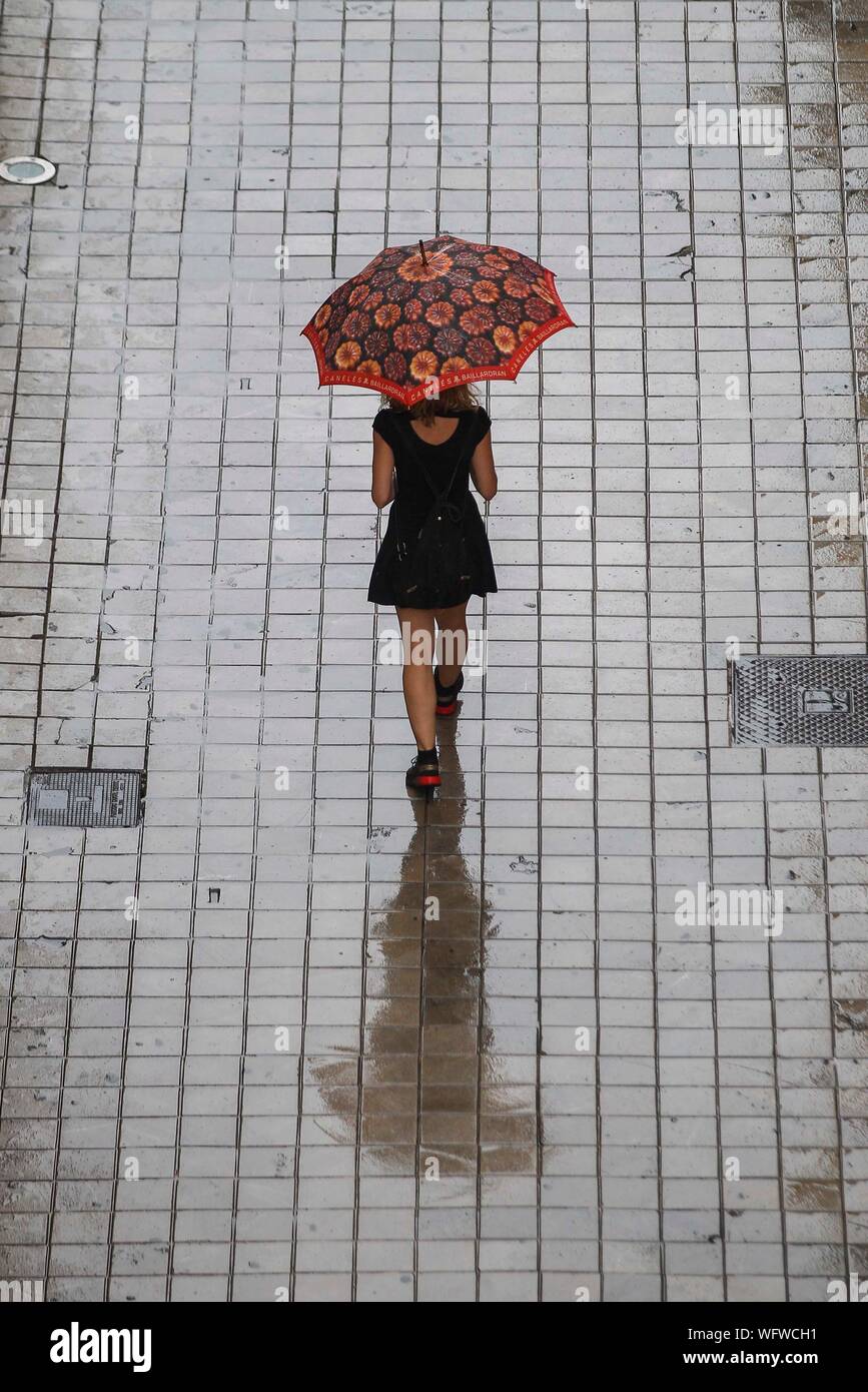 A girl with an umbrella protects herself from the rain on a summer rainy day in Valencia. Stock Photo