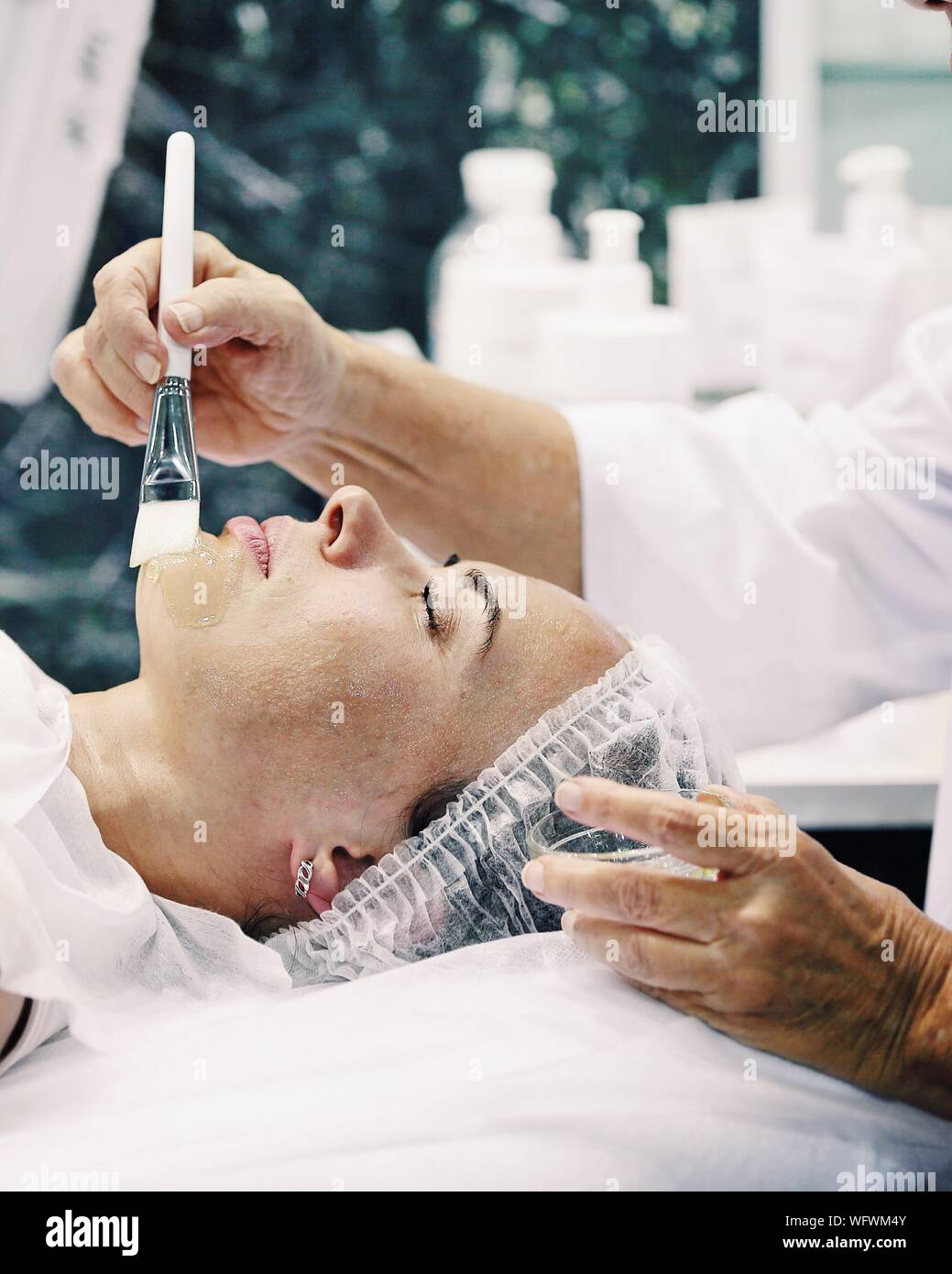 Cropped Hands On Cosmetologist Applying Cream On Female Customer Chin Stock Photo