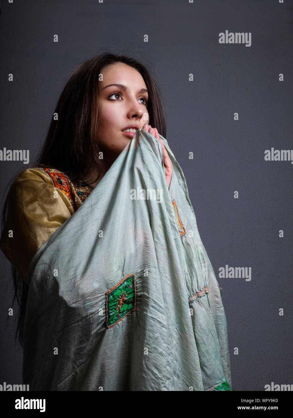 Thoughtful Beautiful Woman Holding Shawl Against Gray Background Stock Photo
