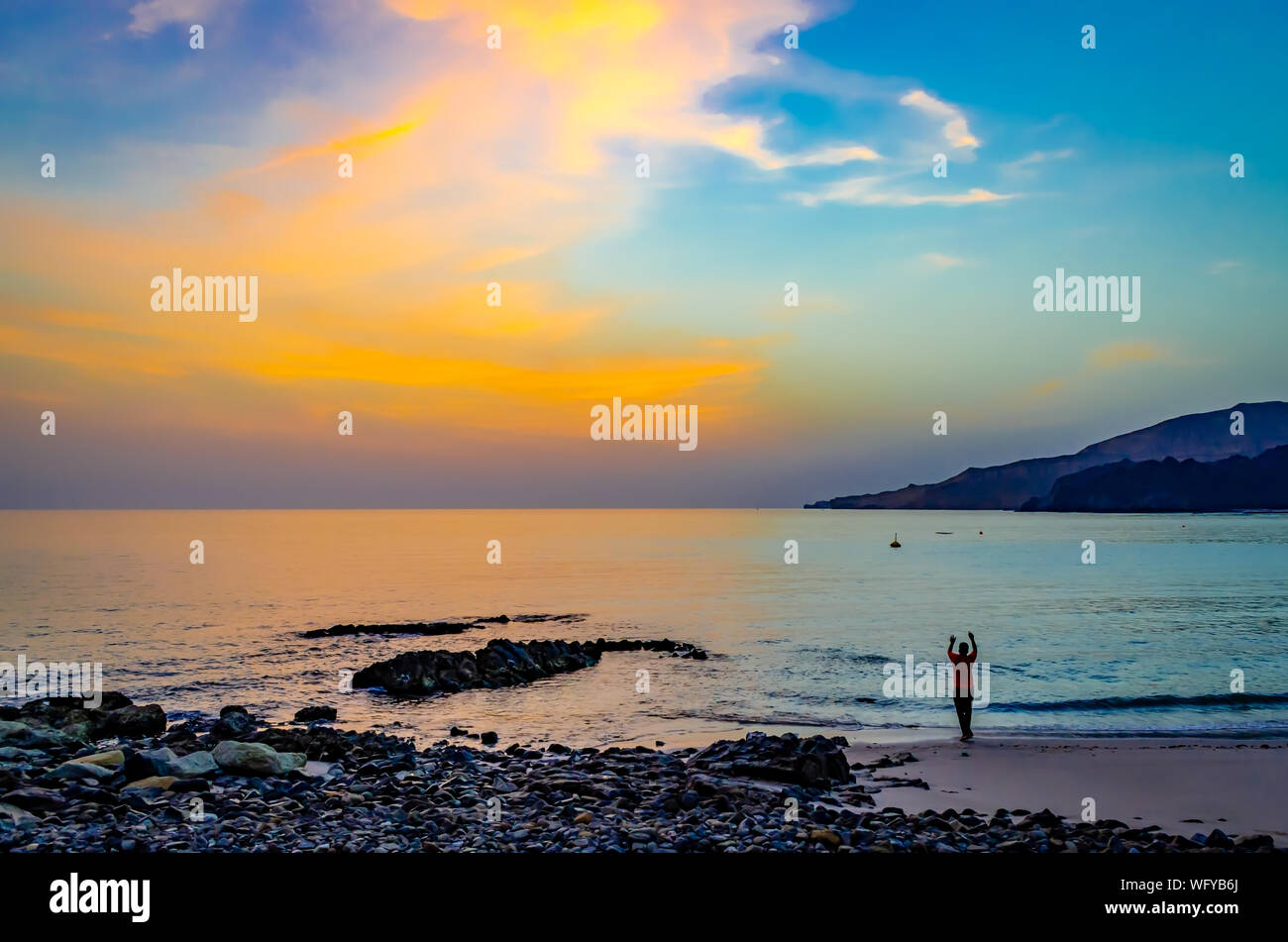 Man doing a yoga pose facing a beautiful sky in the morning on the beach. From Muscat, Oman. Stock Photo