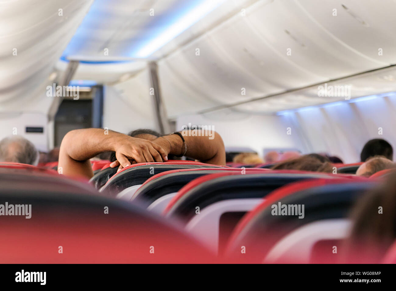 The arms and hands of a passenger watching a movie or resting in the economy cabin class of an airplane flying. Stock Photo