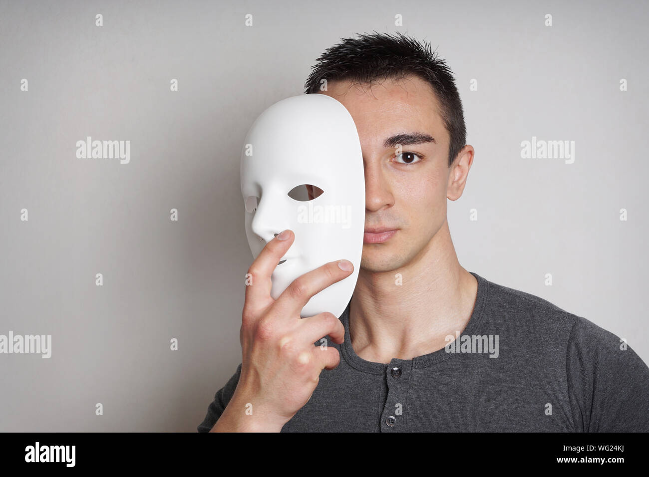 Portrait Of Young Man Holding Mask Against Gray Background Stock Photo ...