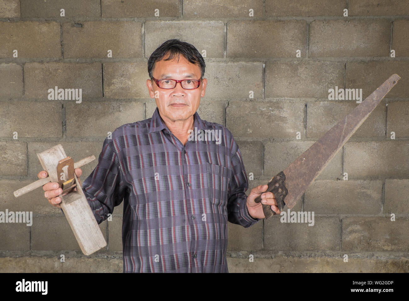 Portrait Of Carpenter Wearing Eyeglasses Holding Work Tools Against Wall Stock Photo
