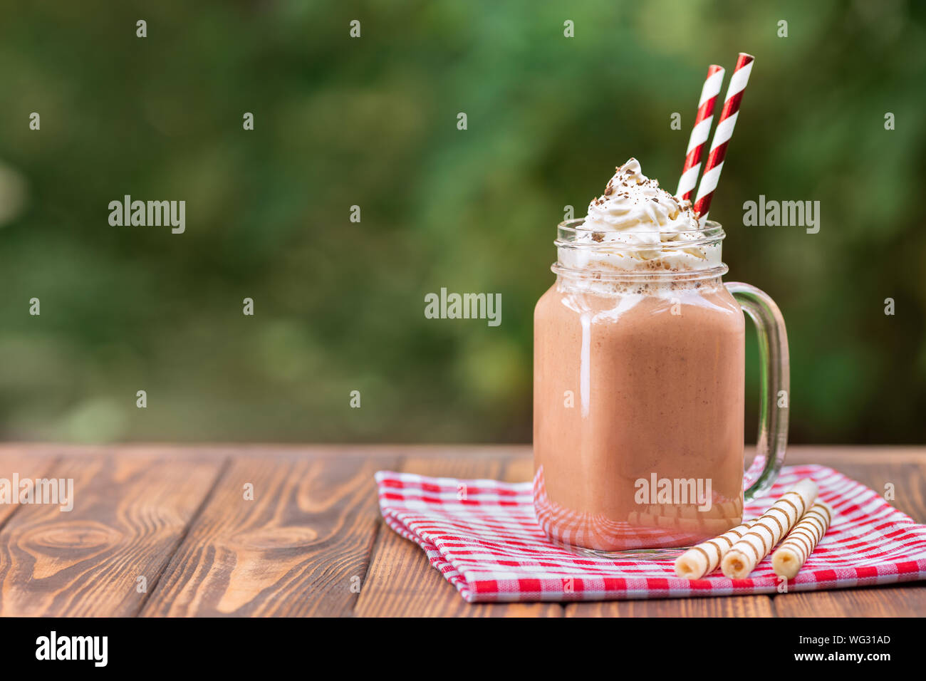 chocolate milkshake in mason jar with whipped cream and wafer rolls on wooden table outdoors Stock Photo