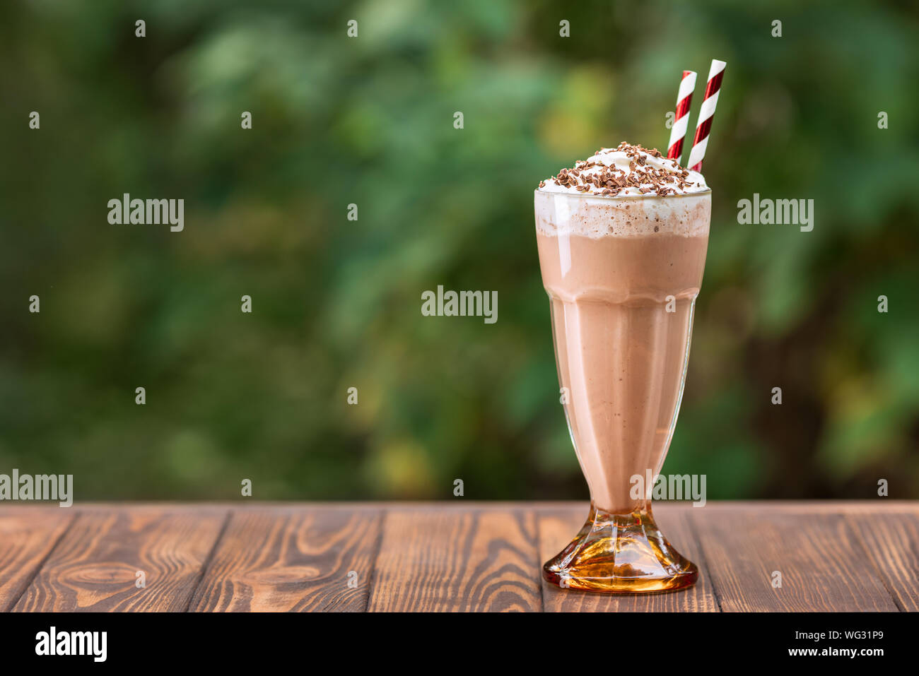chocolate milkshake in glass with whipped cream on wooden table outdoors Stock Photo
