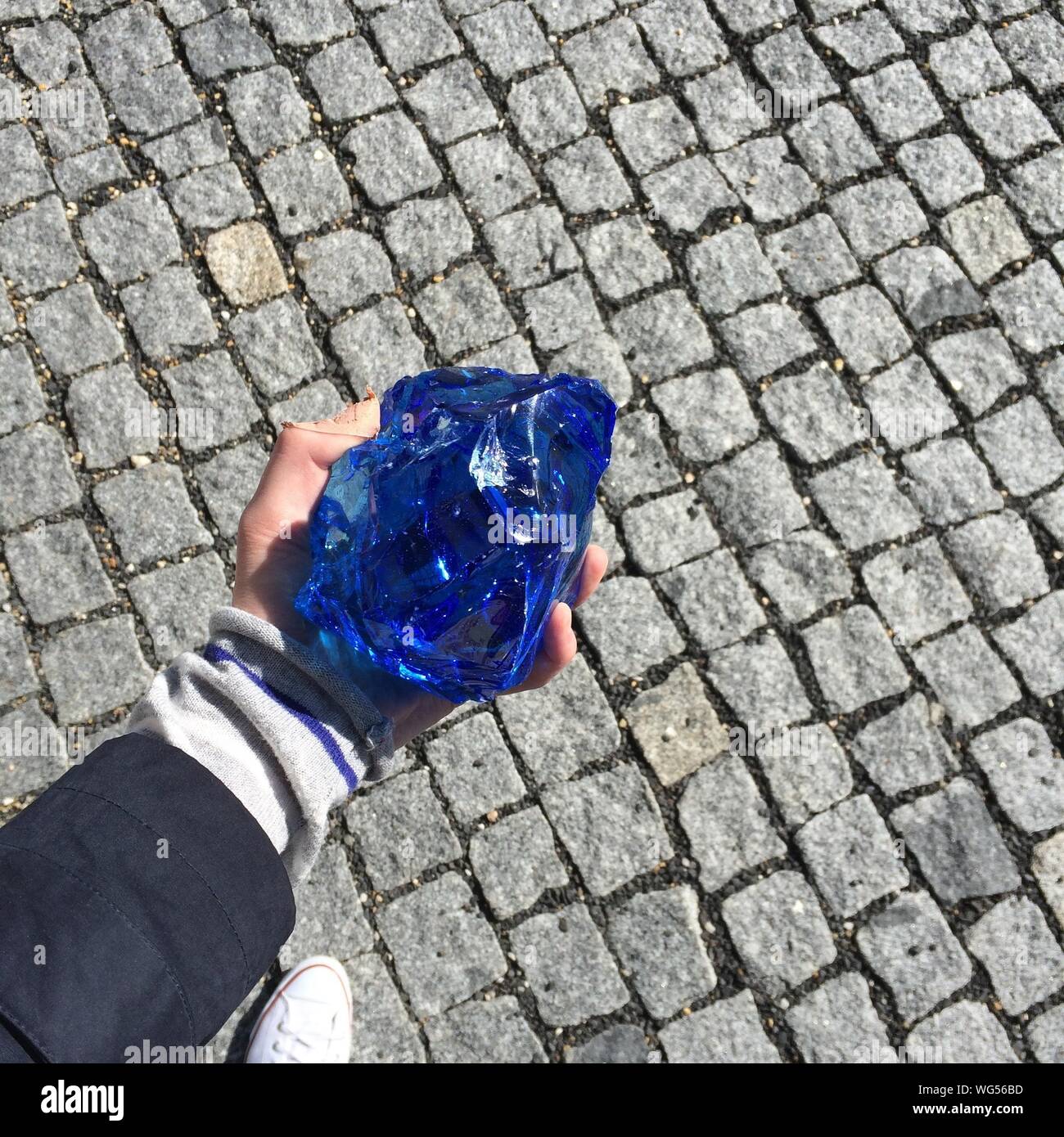 Cropped Hand Of Person Holding Blue Stone On Footpath Stock Photo