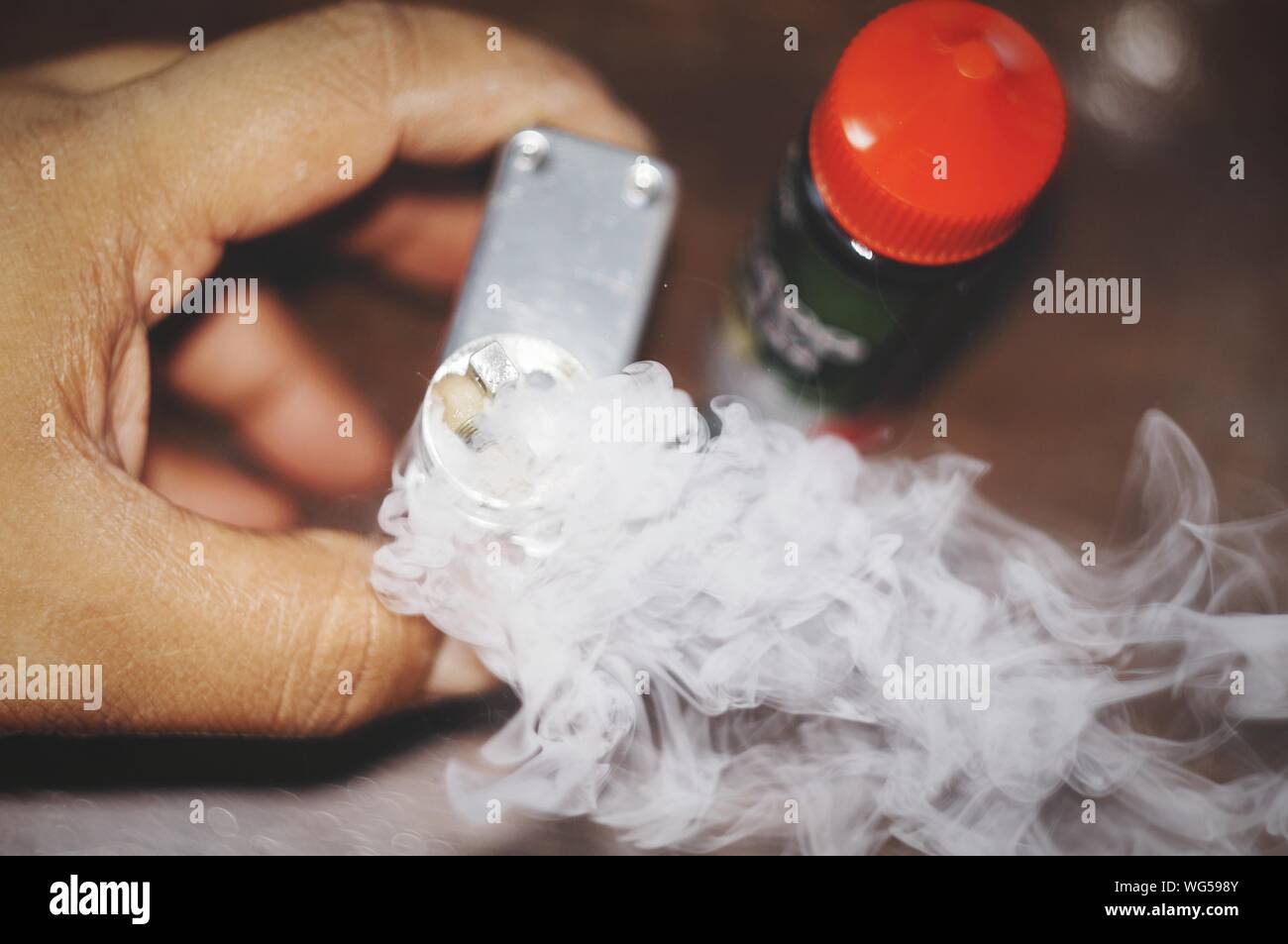 Close-up Of Hand Holding Narcotic Drug With Smoke Emitting From Bottle Stock Photo