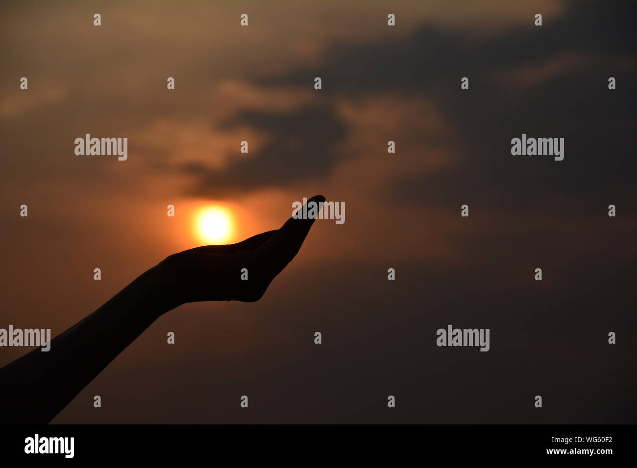 Optical Illusion Of Silhouette Hand Holding Sun Sky During Sunset Stock Photo