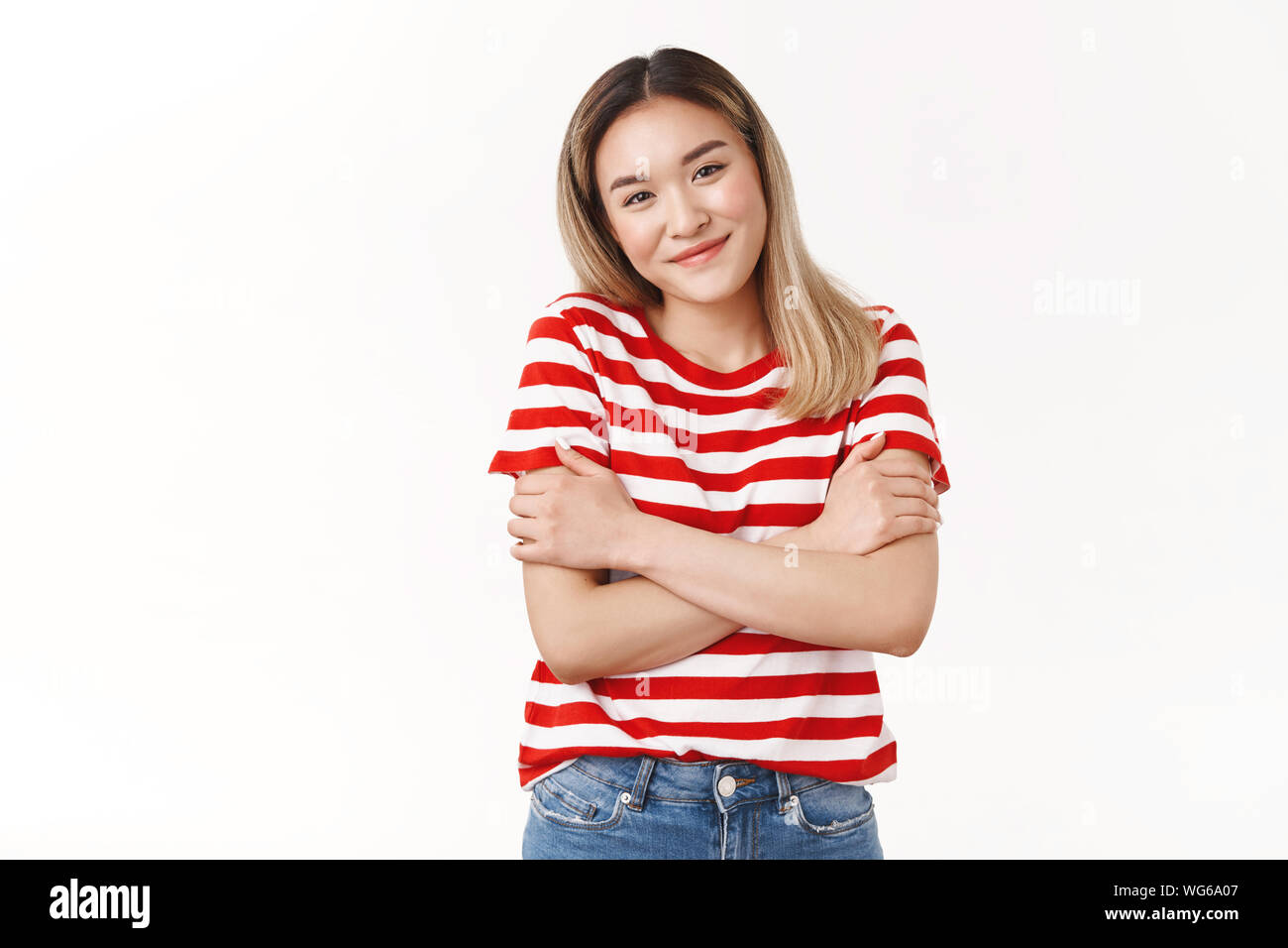 Tender cute asian female wearing striped red t-shirt hugging herself cross arms chest walking evening feel cold chilly smiling kindly glad hanging Stock Photo