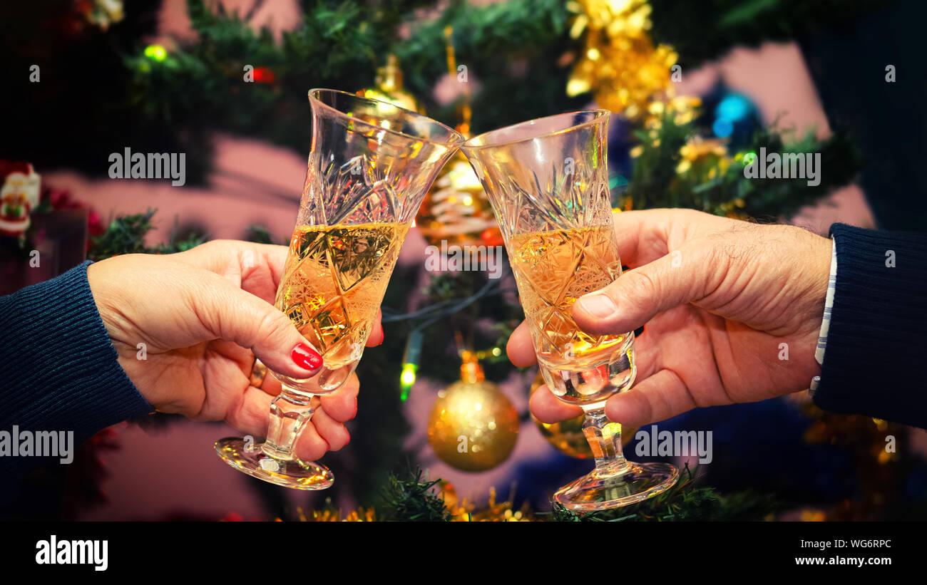 Senior couple hands celebrating Christmas toasting champagne wine at home with decorated Christmas tree in background – winter holiday concept Stock Photo