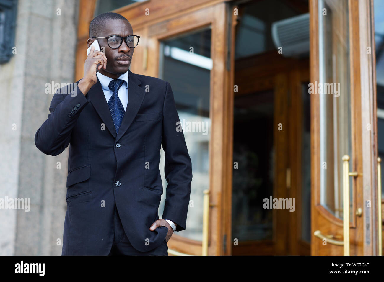 Waist up portrait of stylish African-American man wearing suit speaking by smartphone while leaving work, copy space Stock Photo