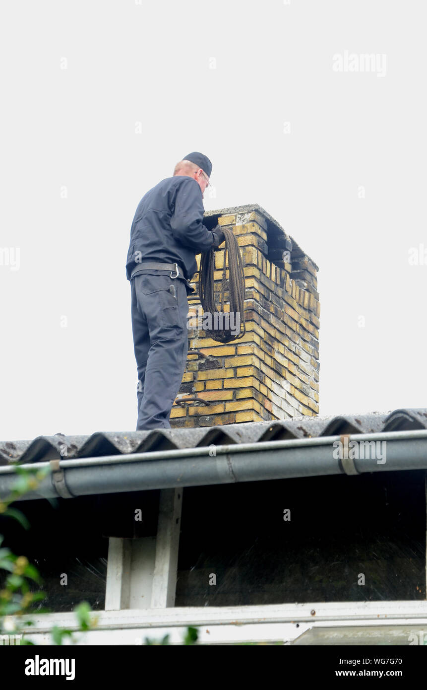 Chimney sweeper at work on a roof with a yellow stone chimney Stock Photo