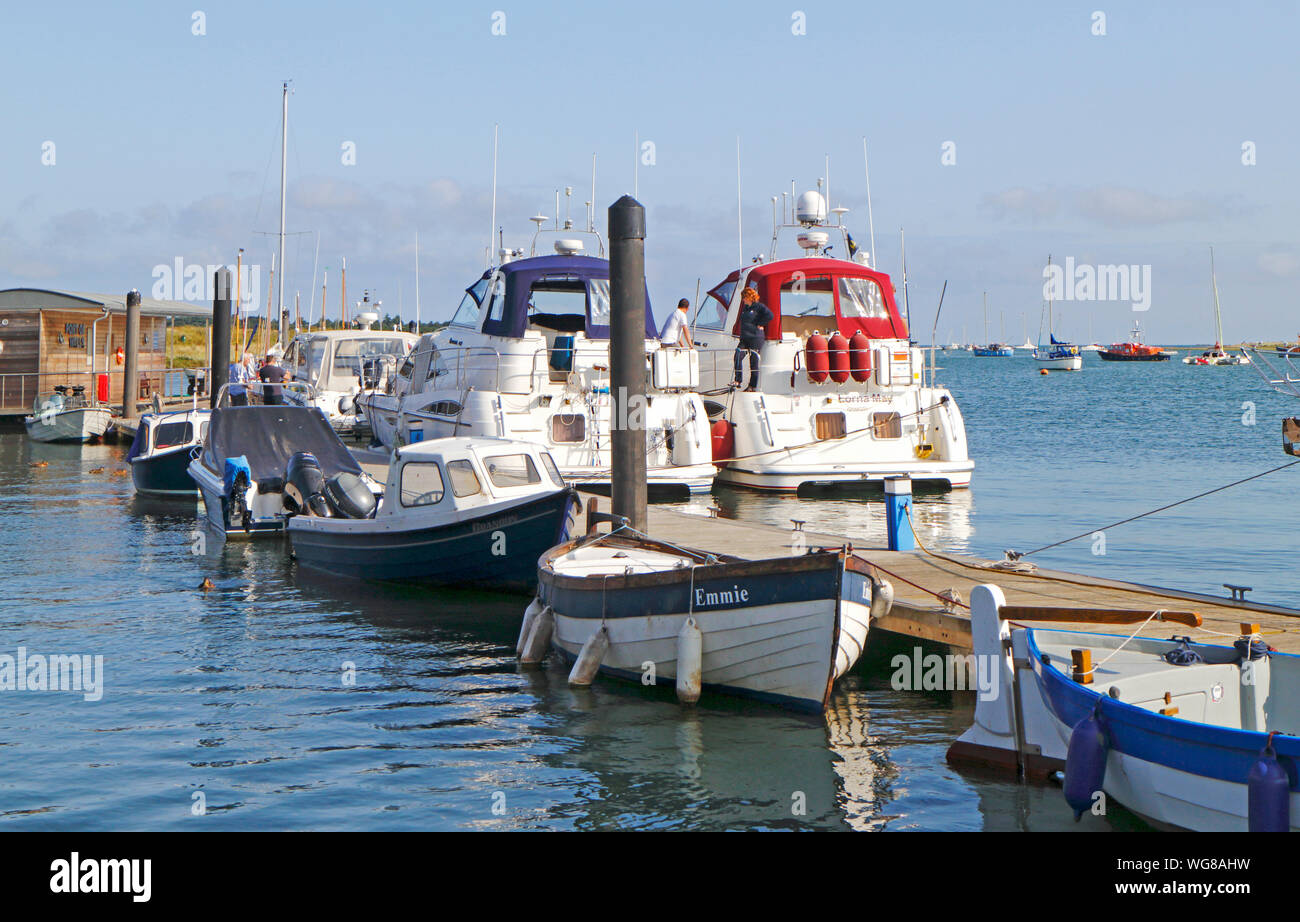 Small boats and luxury cruisers moored to a pontoon at the west end of the harbour at Wells-next-the-Sea, Norfolk, England, United Kingdom, Europe. Stock Photo