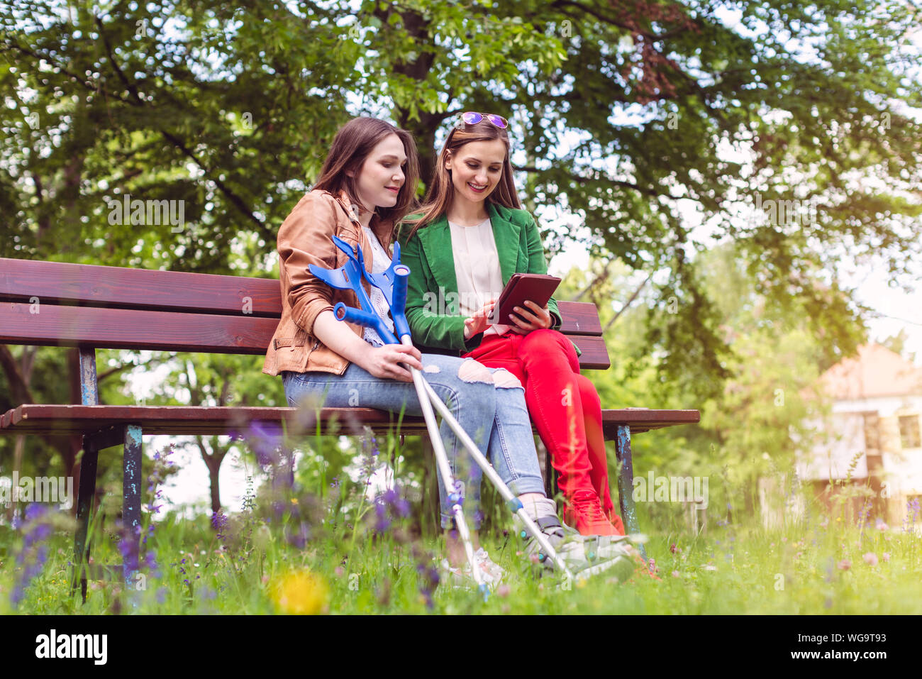 Two friends in a park, one with a broken feet and crutches Stock Photo