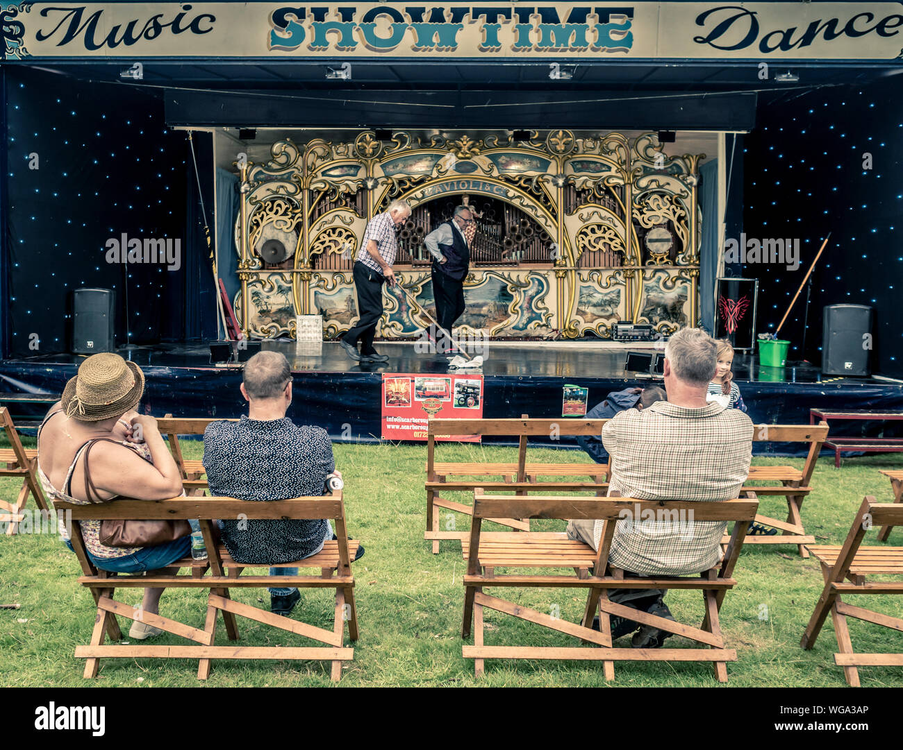 Audience watching stage in front of fairground steam organ being mopped between showers at outdoor show Stock Photo