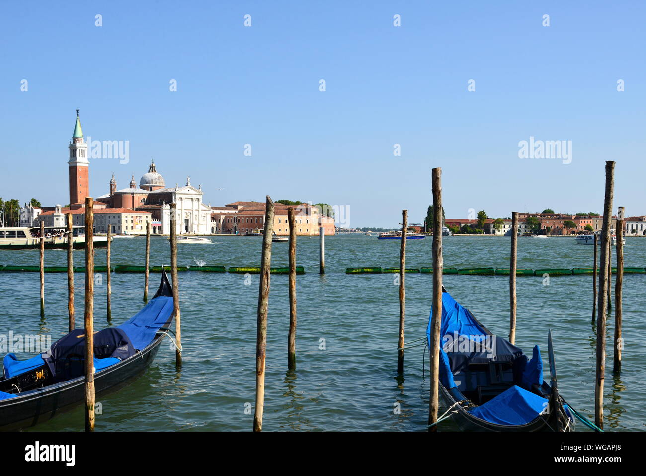 In front view two moored gondolas attached on mooring poles on quay San Marco square. Background San Giorgio Maggiore church Grand Canal Venice Italy Stock Photo