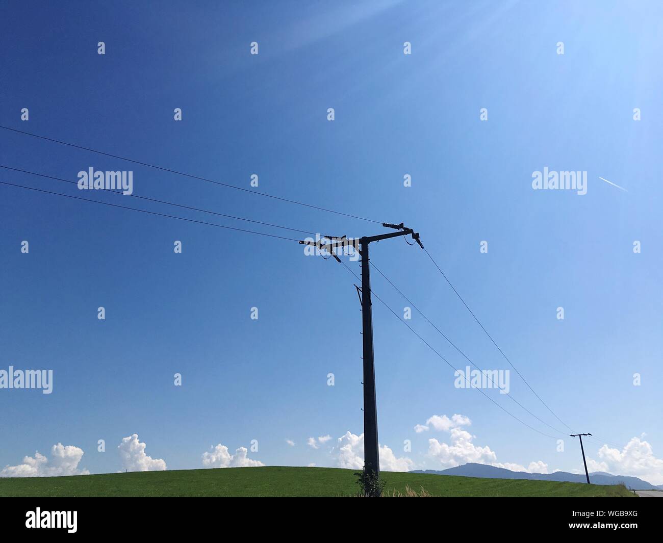 Low Angle View Of Power Line Against Blue Sky On Sunny Day Stock Photo