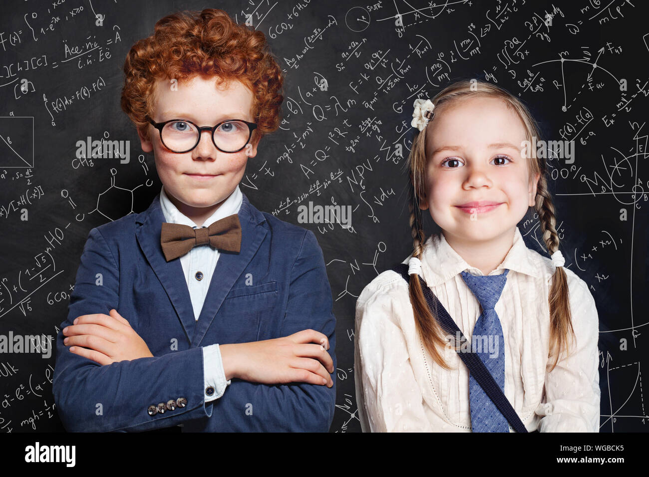 Cute school kids portrait. Little girl and boy school student on blackboard background with science and maths formulas Stock Photo