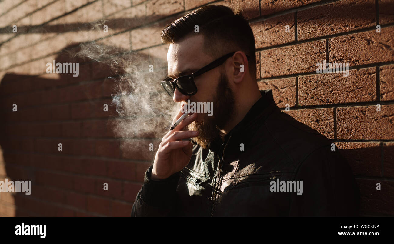 Side view of handsome bearded man smoking a cigarette over brick wall Stock Photo