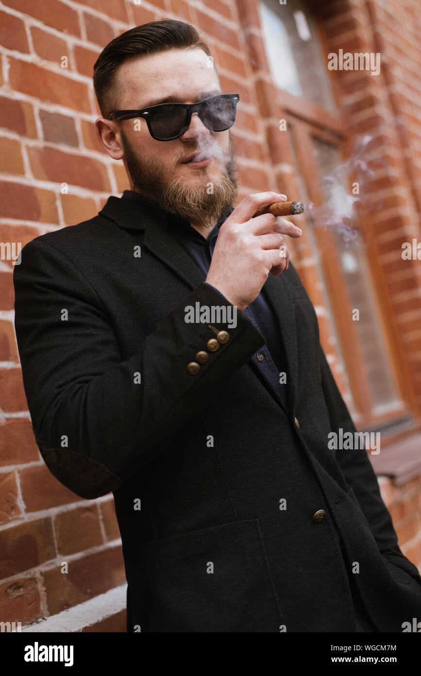Handsome bearded man smoking a cigarette over brick wall Stock Photo