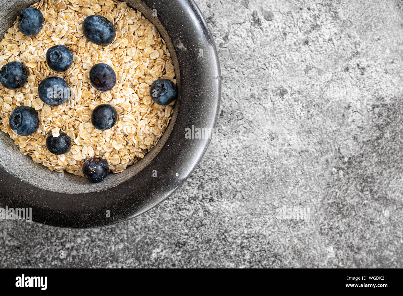 top view of rolled oats, oatmeal and blueberries in stone bowl on kitchen counter Stock Photo