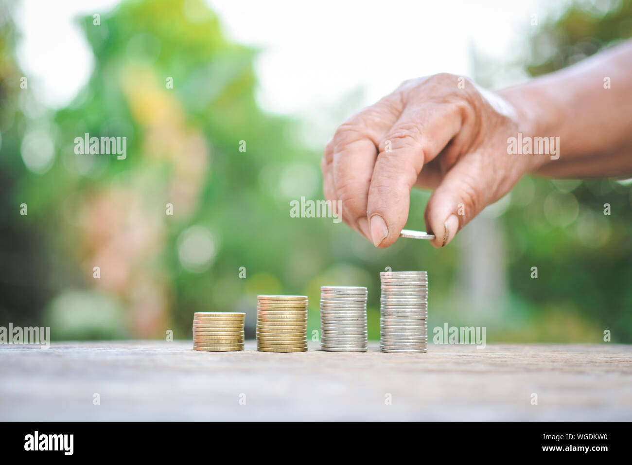 Cropped Hand Arranging Coins On Table Against Trees Stock Photo