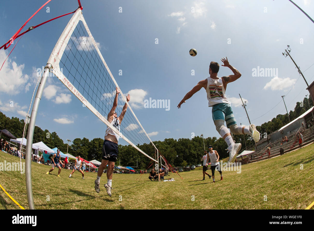 A man jumps high to spike the ball in a triples grass volleyball