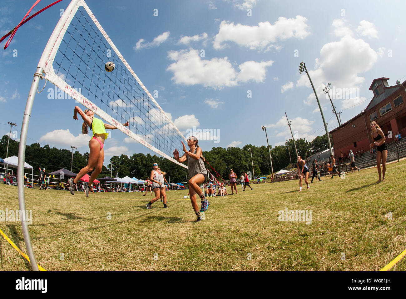 A woman jumps high to spike the ball in a triples grass volleyball