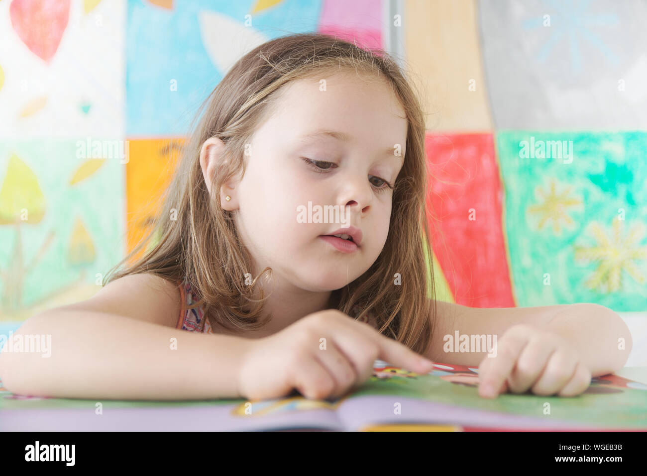 Little girl in a classroom reading a book learning at school. Caucasian student kid in the class at primary education. Stock Photo