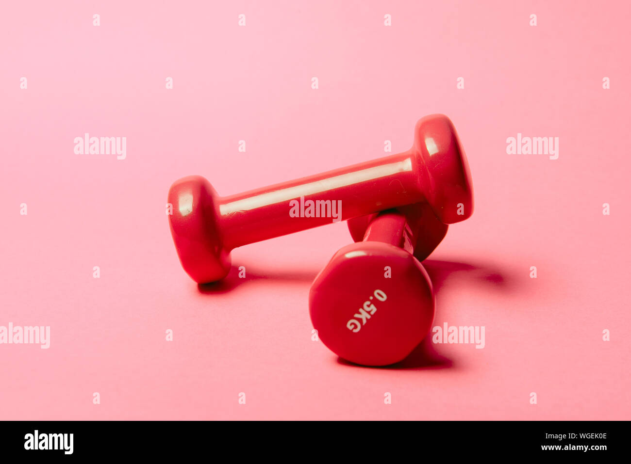 Pair of red 0.5 kg dumbbells on pink paper background. Stock Photo