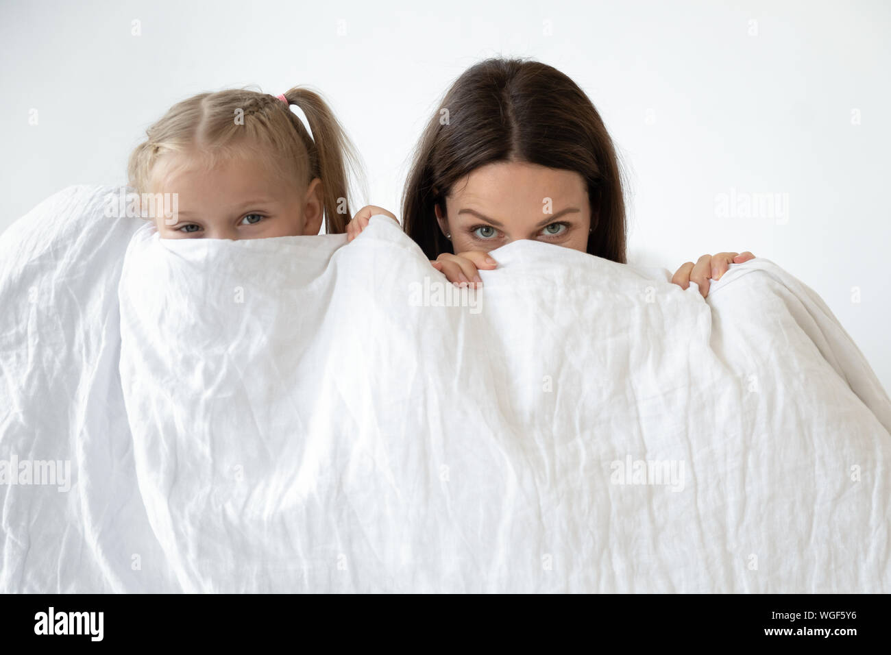 Mother and daughter hiding behind white blanket indoors Stock Photo