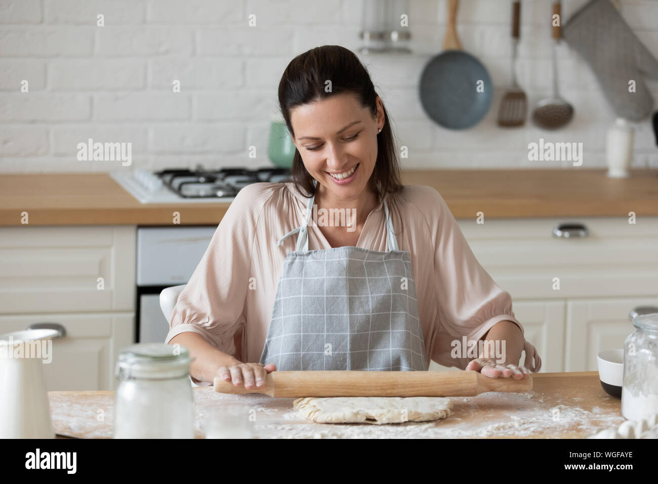 Woman flattening dough with rolling pin in the kitchen Stock Photo