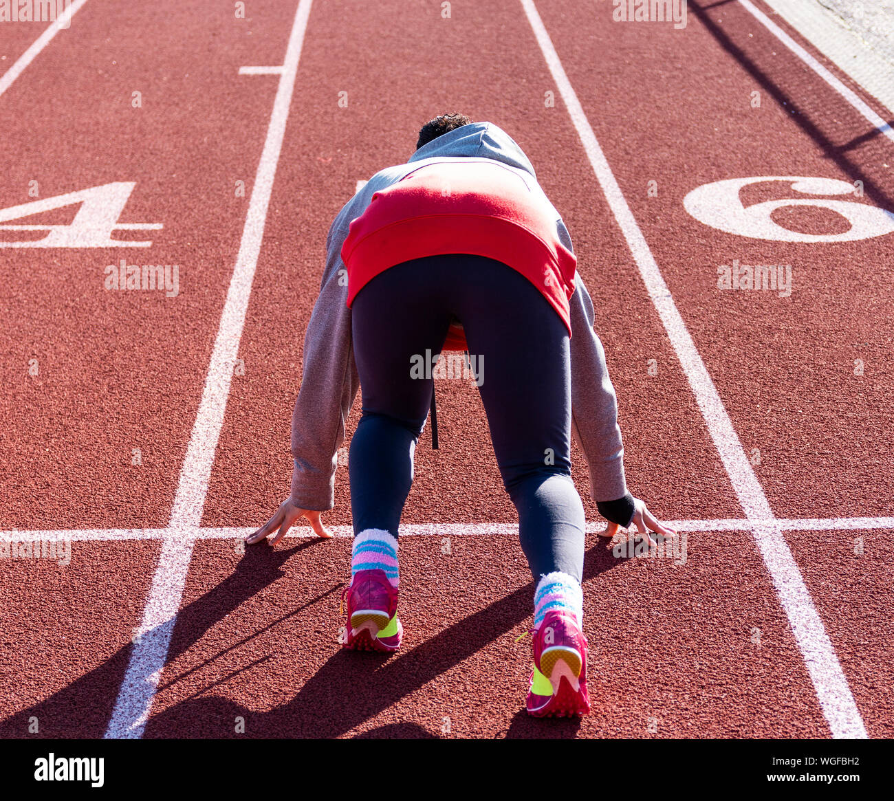 A high school teenage girl is in the set position ready to sprint down the straightway of a track during track and field practice. Stock Photo