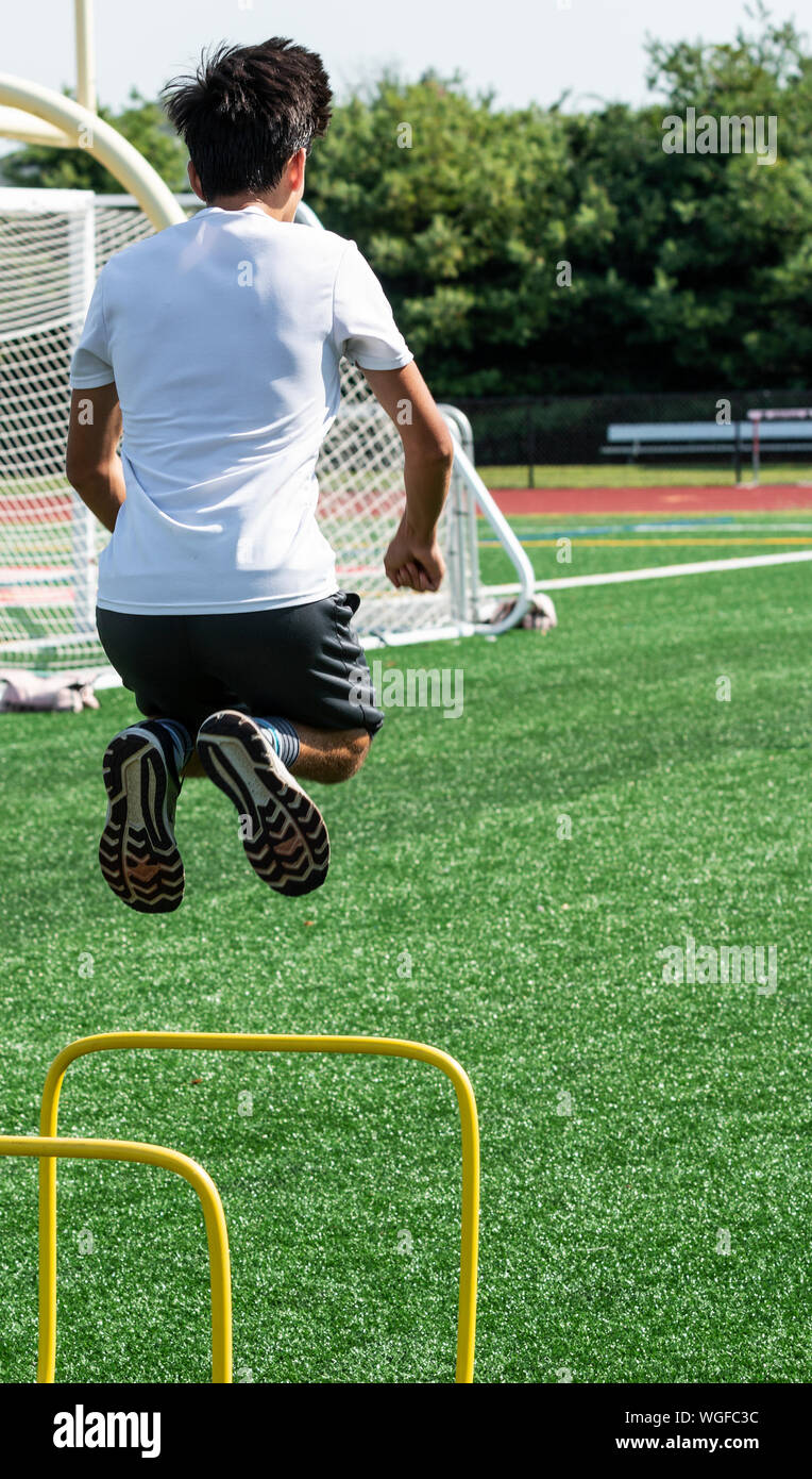A teenage boy is jumping over two foot high yellow hurdles during practice after school. Stock Photo