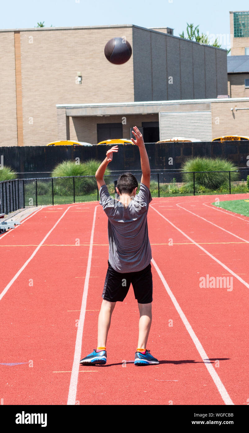 A high school teenage boy is throwing a medicine ball backwards over